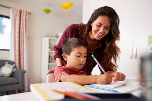 Photo of mother helping her son with homework at a table.